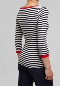 Schwarz-weiße gestreifte Langarmbluse mit roten Akzenten am Kragen und an den Ärmeln, körperbetontes Design, Rückansicht.