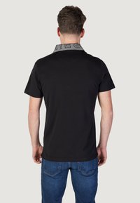 Camiseta negra con un cuello gris y estampado. Diseño de mangas cortas, escote redondo y una textura simple y suave. Jeans de mezclilla visibles por debajo.