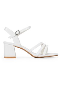 Sandalias de tacón blanco con tacón bloque, que presentan un diseño con tiras y hebilla ajustable en el tobillo. Textura de cuero suave con una suela color marrón.