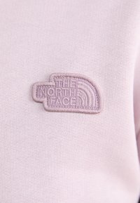 Tessuto viola chiaro con un logo ricamato testurizzato di "The North Face" nello stesso colore, con accenti curvi.