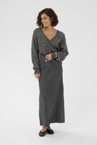 Cardigan gris texturé avec un col en V, porté par-dessus une longue jupe grise. Des chaussures plates noires et un bracelet en argent ajoutent des accents subtils.