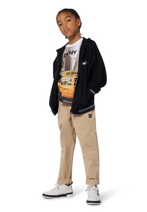Veste zippée noire avec des accents blancs, t-shirt graphique avec des images urbaines, pantalon cargo beige et baskets blanches avec des détails noirs.