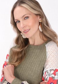 Oliven grøn ribbstretch sweater med mønstrede blomstersleeves; har blonderaccenter og frynseøreringe. Glat tekstur, rund halsudskæring.