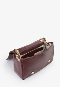 Borsetta in pelle bordeaux con dettagli in oro, superficie testurizzata e chiusura a scatto. Interno dotato di molteplici scomparti per un migliore risparmio di spazio.