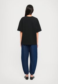 Μαύρο υπερεπίμετρο T-shirt με κοντά μανίκια, συνδυασμένο με φαρδιά σκούρα μπλε τζιν παντελόνια, που διαθέτουν ελαστικούς καρπούς. Απλός σχεδιασμός, χωρίς σχέδια.