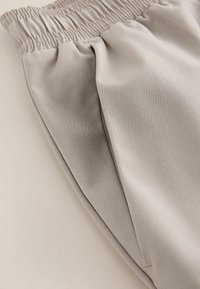Pantalon beige à taille élastique avec poches latérales et texture de tissu lisse, présenté en gros plan sur une surface plane.