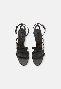 Sorte stroppesandaler med flat såle. Har justerbare ankelremmer og hardware i gulltone med strukturert fotseng.