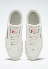 Białe skórzane sneakersy z perforowanym przodem, płaskimi sznurowadłami i czerwono-złotym logo Reebok na języku. Gładka tekstura i niski fason.