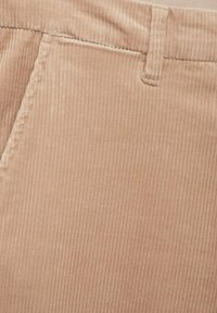 Gros plan sur un tissu en velours côtelé beige avec des rainures verticales visibles, des coutures et une boucle de ceinture sur une poche de vêtement.