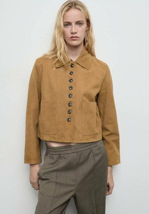 Chaqueta corta de ante marrón con cuello, con cierre de botones en el frente y dos bolsillos delanteros. Textura suave y corte entallado.