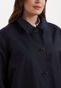 Ναυτικό μπλε παλτό με κλασικό γιακά, κλείσιμο με κουμπιά σε σκούρο χρώμα και λεία υφή. Κατάλληλο για διάφορες περιστάσεις.