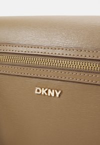 Borsa a mano in finta pelle beige con zip dorata, caratterizzata da una superficie testurizzata e logo DKNY in rilievo sul davanti.