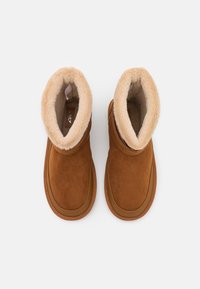 Een paar bruine suède winterlaarzen met een zachte beige bontvoering en rubberen zolen, bekeken vanuit boven op een witte achtergrond.