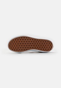 Suela de zapato de goma con una superficie de tracción marrón y un patrón. Bordes laterales blancos y un talón ligeramente elevado. Perfil plano con elementos de diseño geométrico.