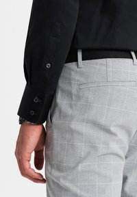 Camicia nera con polsini bottonati, abbinata a pantaloni grigi a quadri con finitura testurizzata e una tasca posteriore singola.
