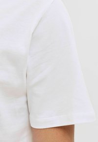 Balta medvilnė marškinėliai su trumpomis rankovėmis. Minkšta tekstūra, standartinis kirpimas. Pasižymi švariu, paprastu dizainu su subtiliu siuvimu palei apačią.