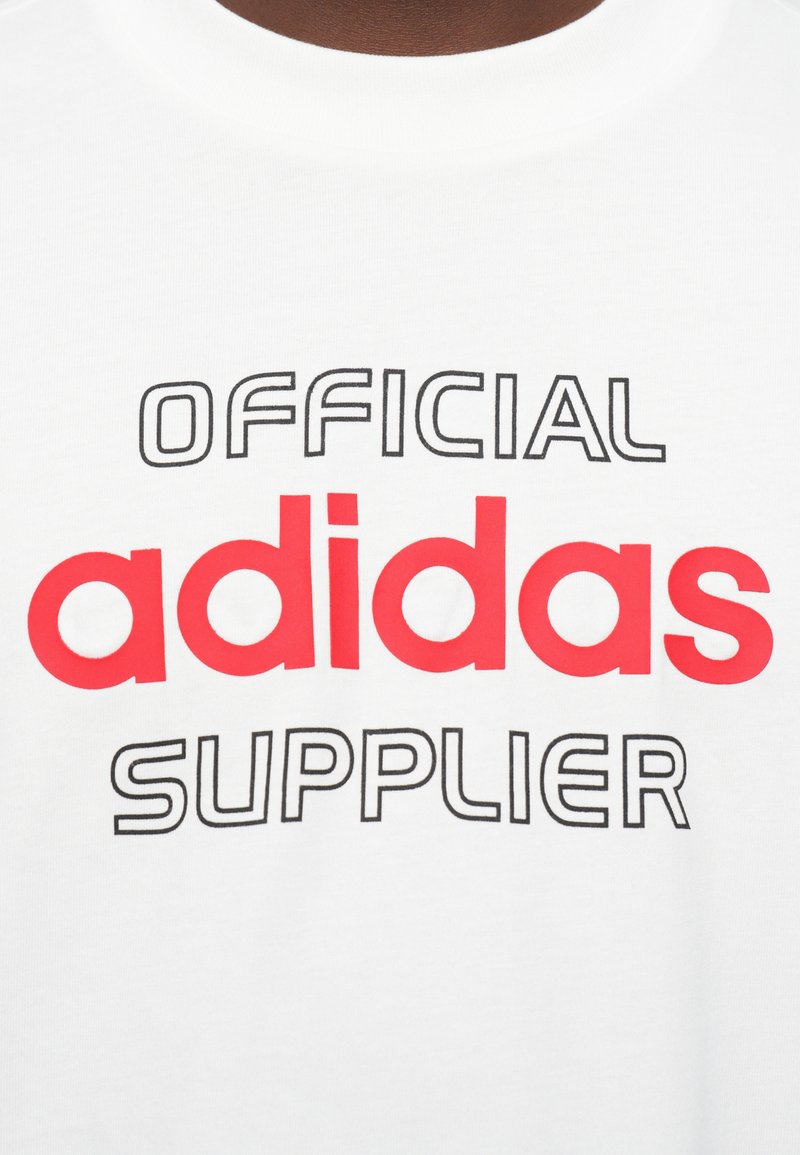 Camiseta blanca con el texto "PROVEEDOR OFICIAL de adidas" impreso, "adidas" en negrita roja y las otras palabras en una fuente de contorno negro delgado.