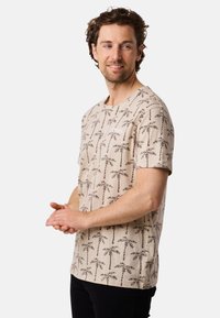 Light beige short-sleeve t-shirt with palm tree pattern, featuring a round neckline and a small logo on the chest. Soft cotton material.