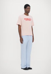 Ροζ βαμβακερή μπλούζα με το λογότυπο "Fiorucci Cash & Carry" σε κόκκινο χρώμα, συνδυασμένη με μπλε και λευκές ριγέ φαρδιές παντελόνες. Απλό, χαλαρό εφαρμοστό.