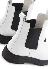 Witte leren Chelsea-boots met een zwart elastische zijpaneel, contrasterende stiksels en een dikke zwarte rubberen zool met profiel.