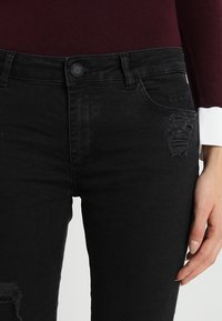 Svarta jeans i denim med slim fit, hög midja, slitage detaljer och vanlig knappstängning. Materialet verkar släta och hållbart.
