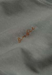 Graum stoff mit einer glatten textur zeigt ein gesticktes braunes schriftlogo. Das design hat ein einfaches, minimalistisches erscheinungsbild.