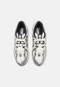Weiße und graue Sportschuhe aus Mesh- und synthetischen Materialien, mit einem strukturierten Design, Schnürsenkeln und reflektierenden Akzenten.