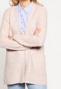 Vaaleanpunainen neulecardigan, jossa on avonainen etuosa, ribattu hihansuu ja hillitty pystyrakenne, päällä vaaleansininen nappipaita.