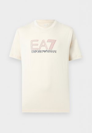 Tricou cu mânecă scurtă, de culoarea crem, cu logo-ul „EA7 Emporio Armani” în text stilizat roșu și negru, centrat pe piept.