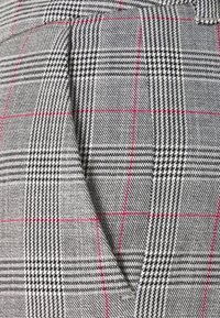 Geweven stof met een zwart, wit en grijs ruitpatroon, geaccentueerd door dunne rode lijnen; textuur met een houndstooth-detail.