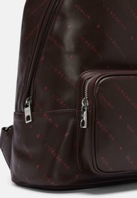 Zaino in pelle marrone scuro con tasca frontale con zip, zip in argento, e motivo testuale rosso "Liebeskind Berlin" sulla superficie.