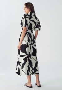 Schwarz-weißes Midi-Kleid mit Blattmuster, das über Puffärmel, eine taillierte Taille und einen fließenden Rock verfügt. Leichter Stoff mit glatter Textur.