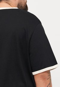 Zwarte t-shirt met een ronde halslijn voorzien van een crèmekleurige rand en crèmekleurige accenten op de mouwen, gemaakt van een glad, gestructureerd stof.