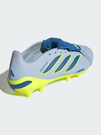 Chaussure de football blanche et jaune néon avec accents bleus, lacets cachés sous une bride, étiquetée "Predator" avec des crampons visibles pour gazon artificiel.