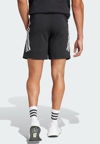 Pantaloni sportivi neri con strisce laterali bianche, vita elasticizzata e texture liscia. Indossati con scarpe da ginnastica bianche e calzini a strisce.