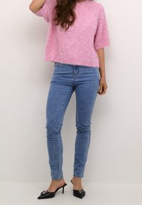 Maglione corto a maniche corte rosa fluffy abbinato a jeans azzurri attillati e mule nere a punta con tacco con dettagli decorativi.