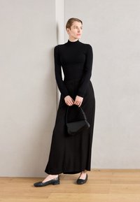 Crna uska rolka, crna suknja do poda visokog struka, crne stanovane cipele s metalnim detaljima i mala crna tašna. Glatke teksture, minimalistički dizajn.