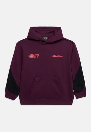 Lila Kapuzenpullover mit schwarzen Ellbogenflicken, vorderer Kängurutasche und zwei kleinen orangefarbenen Logos auf der Brust, eines mit Flammendesign.