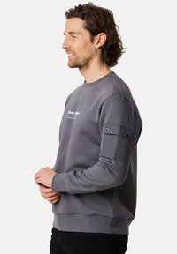 Felpa grigia con collo a giro, caratterizzata da un patch testurizzato sulle maniche e stampa del logo. Il tessuto morbido e i polsini a costine completano il design.