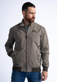 Khaki bomber bunda s stojatým límcem, zapínáním na zip, dvěma bočními kapsami, hnědými žebrovanými manžetami a diskrétním logo nášivkou na hrudi.