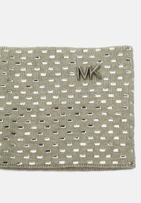 Bolsita de tela tejida en color beige con recortes rectangulares y acentos metálicos. Decorada con el logo plateado "MK". Textura suave.