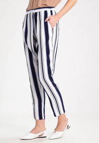 Pruhované kalhoty s námořnickými a bílými svislými pruhy, s volnějším střihem, kapsami a lehkým materiálem. Doplňují je bílé baleríny.