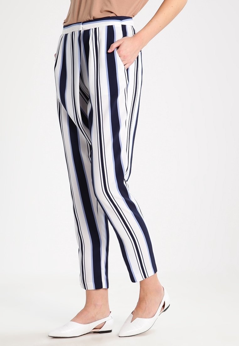 Pruhované kalhoty s námořnickými a bílými svislými pruhy, s volnějším střihem, kapsami a lehkým materiálem. Doplňují je bílé baleríny.