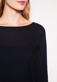 Czarny sweter z dzianiny z szerokim dekoltem, prążkowaną teksturą i długimi rękawami. Materiał, który nie gniecie się, gładko opada na ramionach.