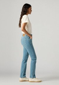 Jeans de un azul claro con diseño de pierna recta, talle medio y detalles de costura sutiles. Combinados con una camiseta de manga corta color crema.