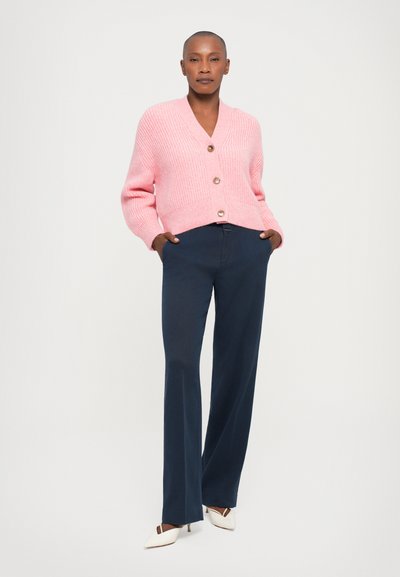 Pink chunky knit cardigan with a V-neck and three buttons, paired with navy wide-leg trousers and cream pointed-toe heels.