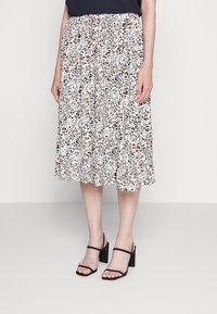 Jupe midi à imprimé léopard en blanc, avec des nuances de brun et de noir. Taille élastique. Portée avec des sandales à talons carrés noires.