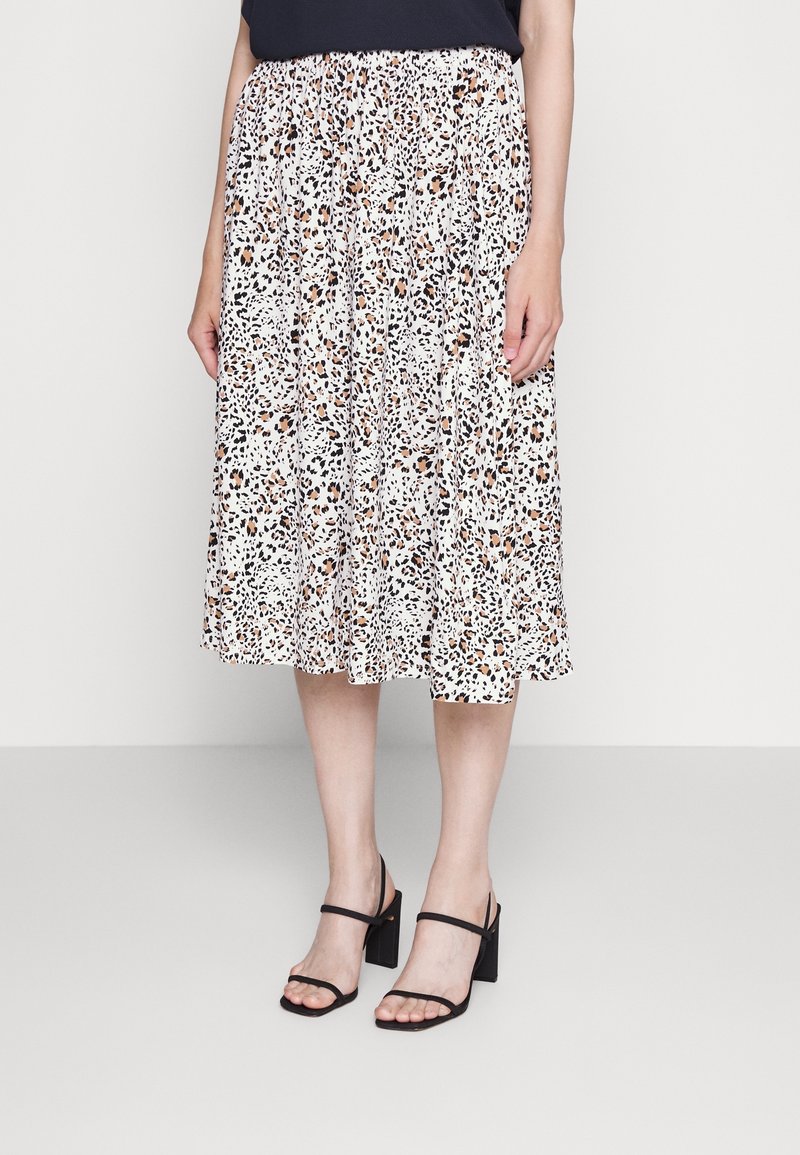 Jupe midi à imprimé léopard en blanc, avec des nuances de brun et de noir. Taille élastique. Portée avec des sandales à talons carrés noires.