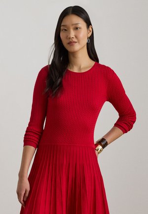Rød strikket kjole med ribbet tekstur, lange ermer og plissett skjørt. Har rund hals og glatt finish med minimale dekorasjoner.