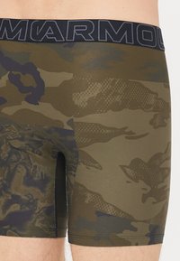 Green patterned boxer shorts featuring a textured fabric, a fitted design, and a black waistband with "ARMOUR" lettering.